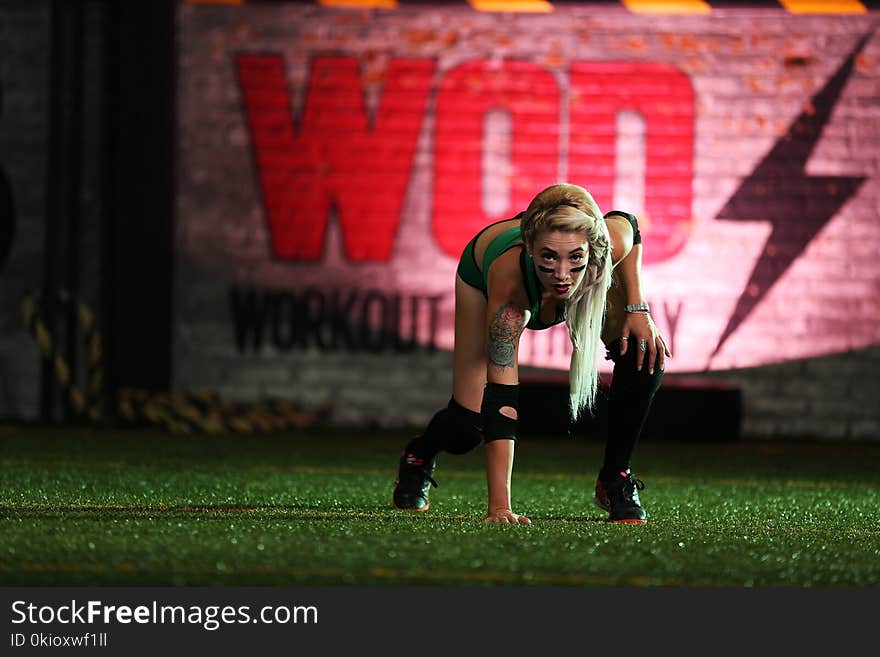 Photo of Woman Wearing Green Top and Black Shorts Touching Grass