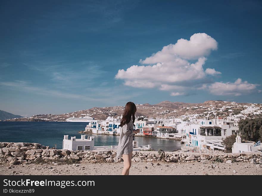 Woman Wearing Gray Shirt Standing in Front White Houses Beside Body of Water