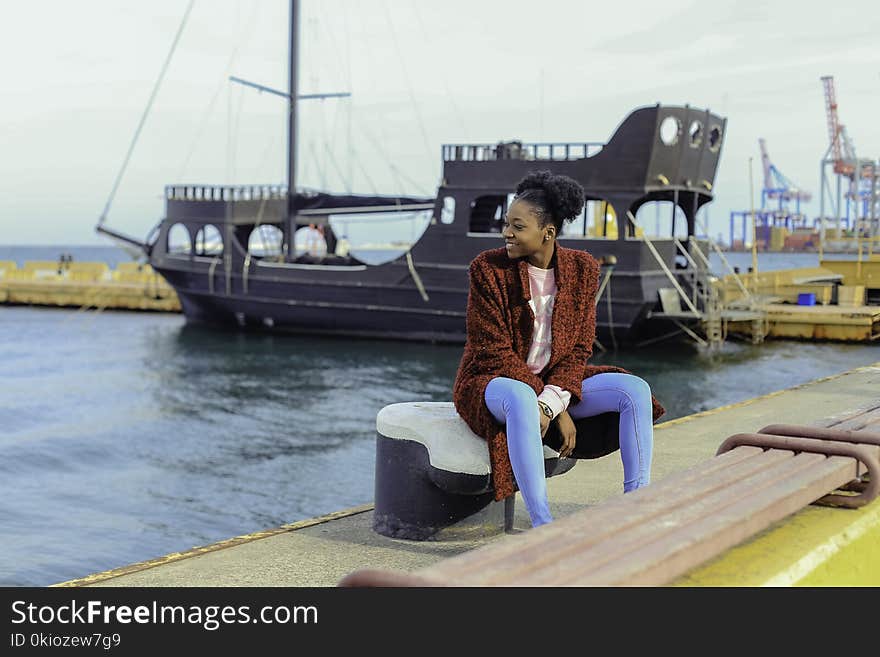 Woman in Red Cardigan Sitting on Black Metal Near Boats