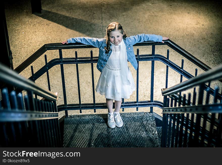 Girl Wearing Blue Jacket and White Dress Standing on Railings during Night Time