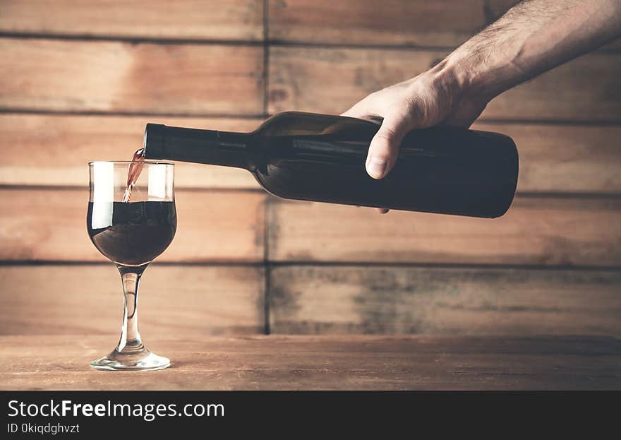 Hand pouring red wine into a glass on a wood background