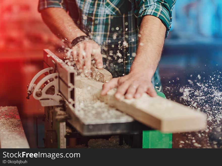 Carpenter builder saws with a circular saw a wooden board on a wooden table in the workshop.