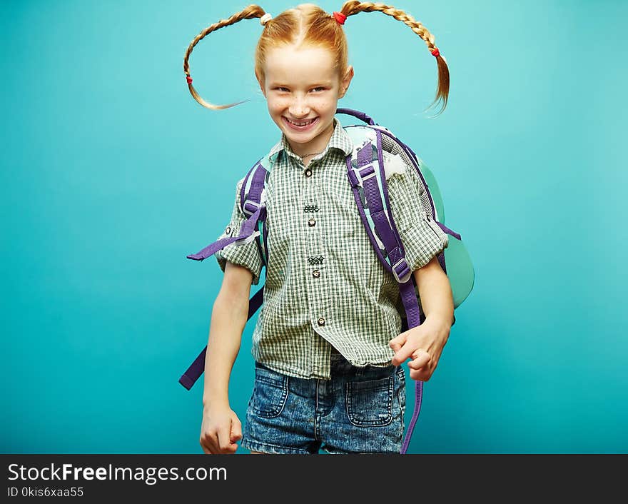 Cheerful girl with backpack on her shoulders happily jumping on blue background.