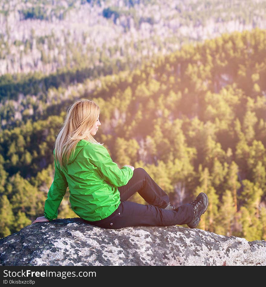 Young woman sitting on cliff`s edge.