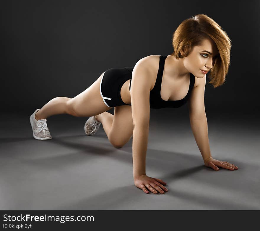 Beautiful young woman doing push-ups on a dark background