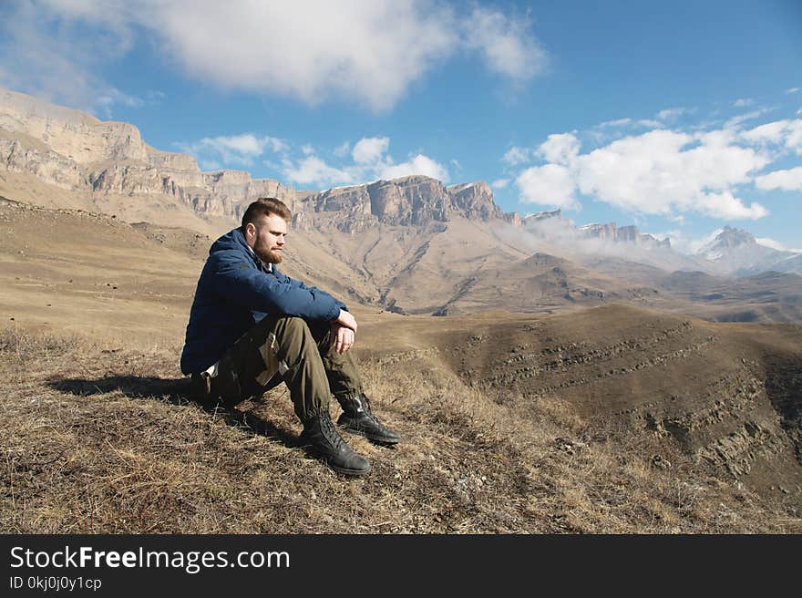 A portrait of a stylish bearded hipster sitting on a rock against the backdrop of epic rocks and contemplating into the