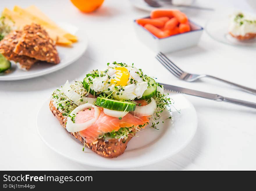 Cereal bun with egg benedict, smoked salmon, sprout micro greens, onion and cucumber slices, cream cheese on the served white wood