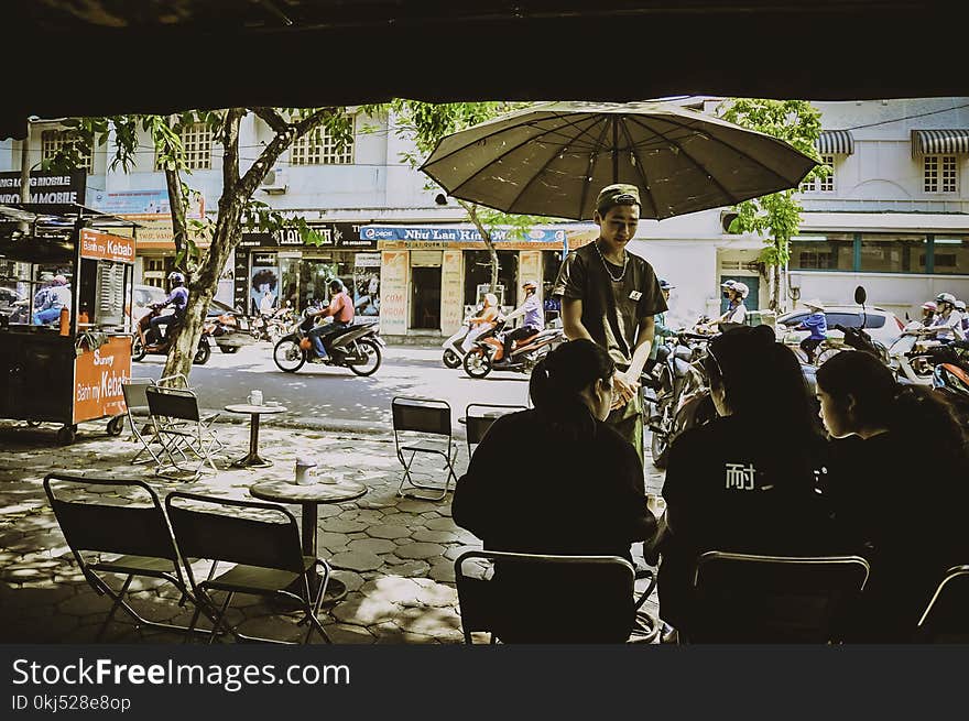 Man Standing Beside Umbrella Facing Three Women Sitting On Chairs