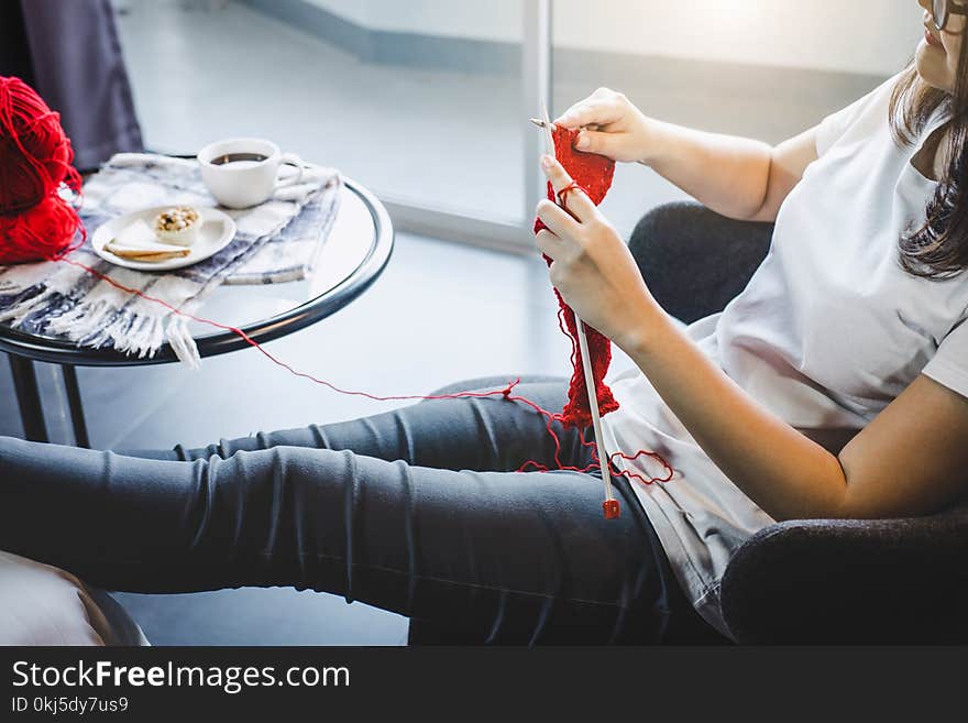 Close up shot of young woman hands knitting a red scarf handicraft in the living room on terrace at home.