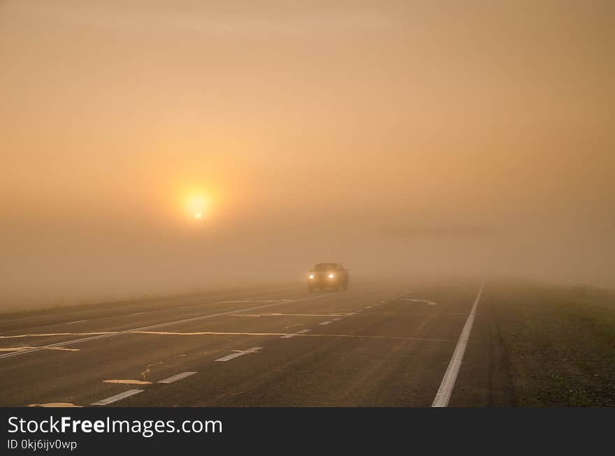 The light from the car`s headlights traveling along the road in the mist outside the city. The light from the car`s headlights traveling along the road in the mist outside the city