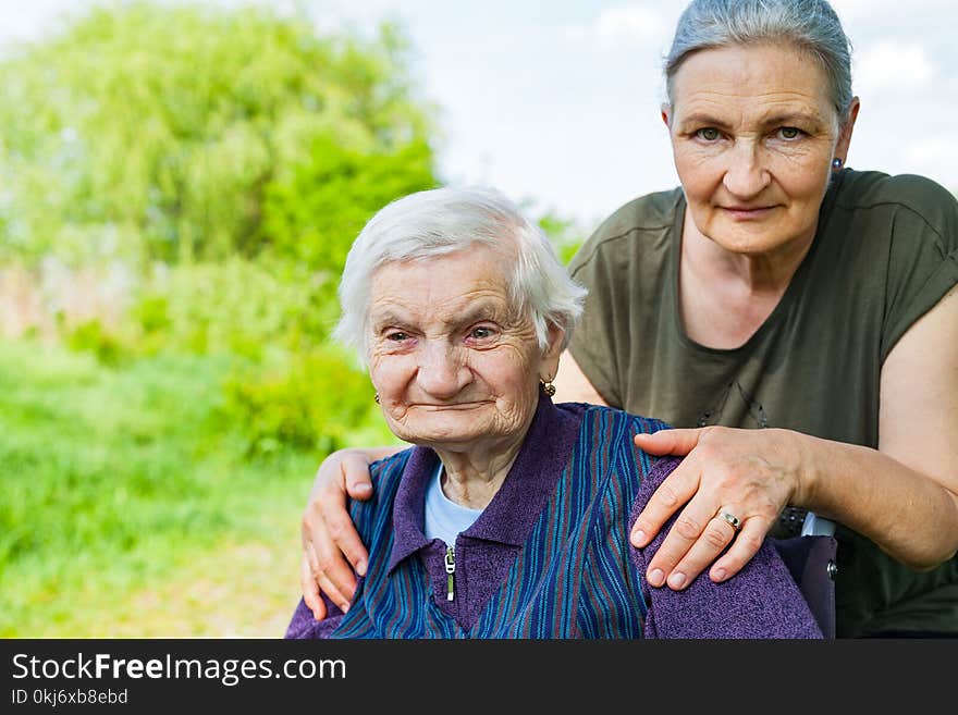 Senior woman with alzheimer disease sitting in wheelchair, posing with her daughter in the park. Senior woman with alzheimer disease sitting in wheelchair, posing with her daughter in the park