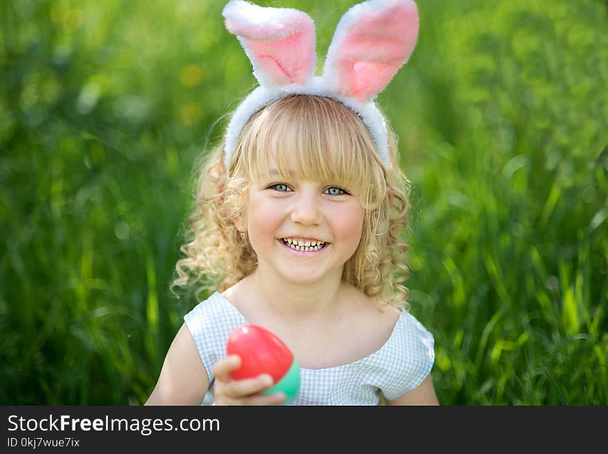 Cute funny girl with Easter eggs and bunny ears at garden. easter concept. Laughing child at Easter egg hunt