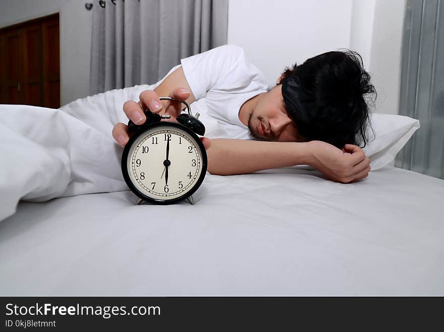 Young Asian man turn off alarm clock on the bed in morning.