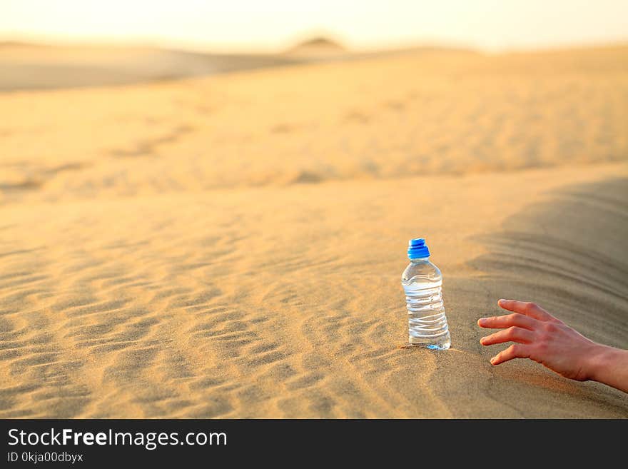 Hand try to catch the bottle of water on sand desert in hot temperature. Concept of to die of thirst.