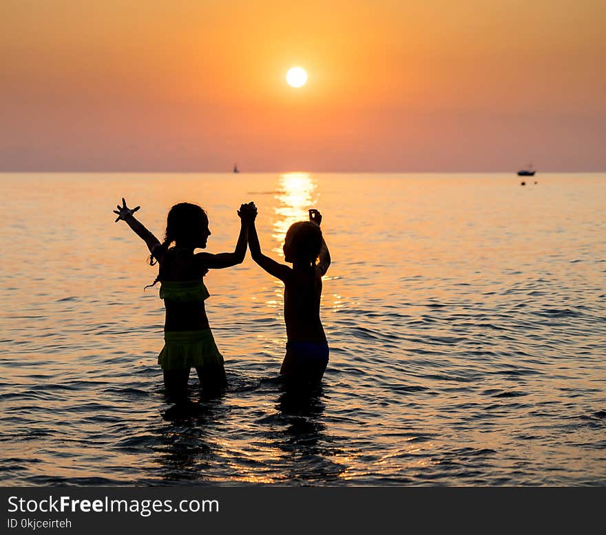 Silhouette of two happy little young girls jumping in sea at sunset. Silhouette of two happy little young girls jumping in sea at sunset