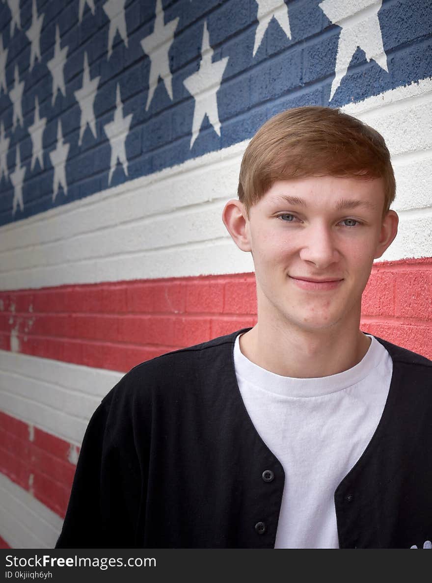 Caucasian teenage boy in front of a brick wall that has an American flag painted on it. Caucasian teenage boy in front of a brick wall that has an American flag painted on it.