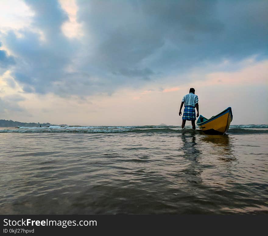 Man on Body of Water Beside Yellow and Blue Boat