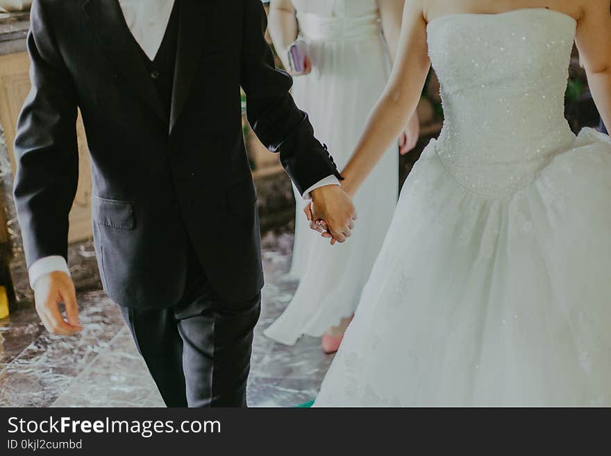 Woman Wearing White Wedding Gown Holding Hands With Man While Walking