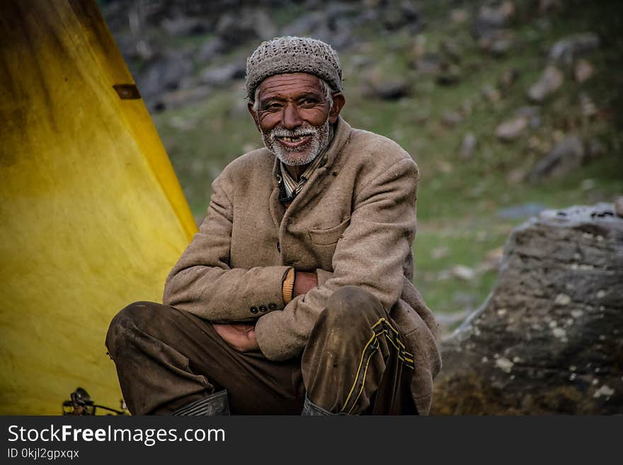 Smiling Man Wearing Gray Knit Cap Sitting Near Gray Rock