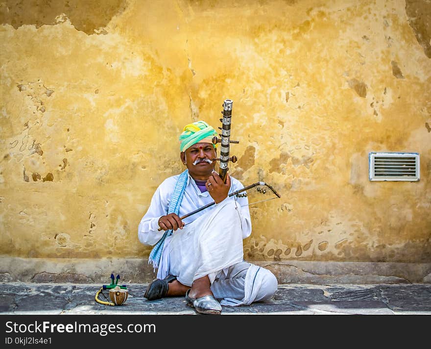 Man Holding String Instrument While Sitting on Concrete Pavement