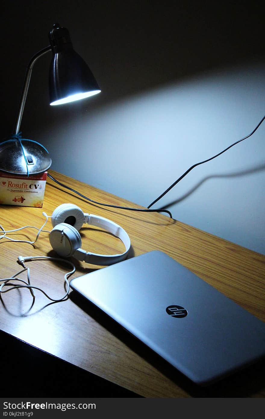 Gray Hp Laptop and White Corded Headphones on Brown Wooden Table