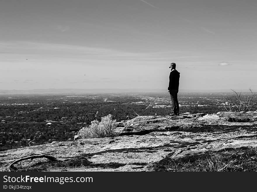 Greyscale Photography of Man Standing on Cliff in Front of Building