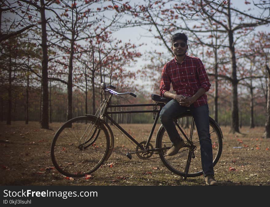 Man Wearing Red Dress Shirt and Blue Jeans Sitting on Black Bicycle