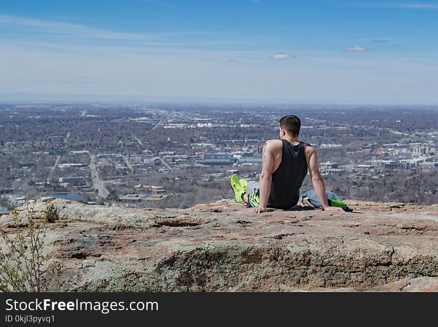 Man Wearing Black Tank Top Sitting Near Edge of Cliff