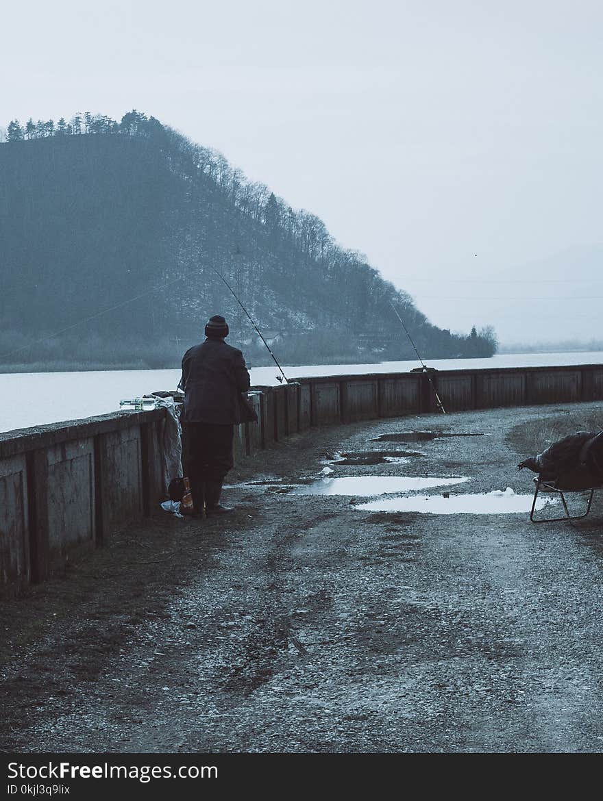 Man Wearing Brown Coat Near a Body of Water With Fishing Rods at Daytime