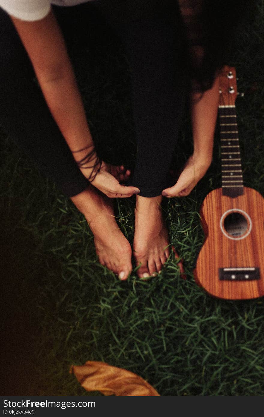 Person Sitting on Green Grass Field Beside Ukulele