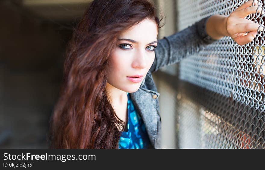 Woman Wearing Gray Denim Jacket Leaning on Gray Chain Link Fence at Daytime