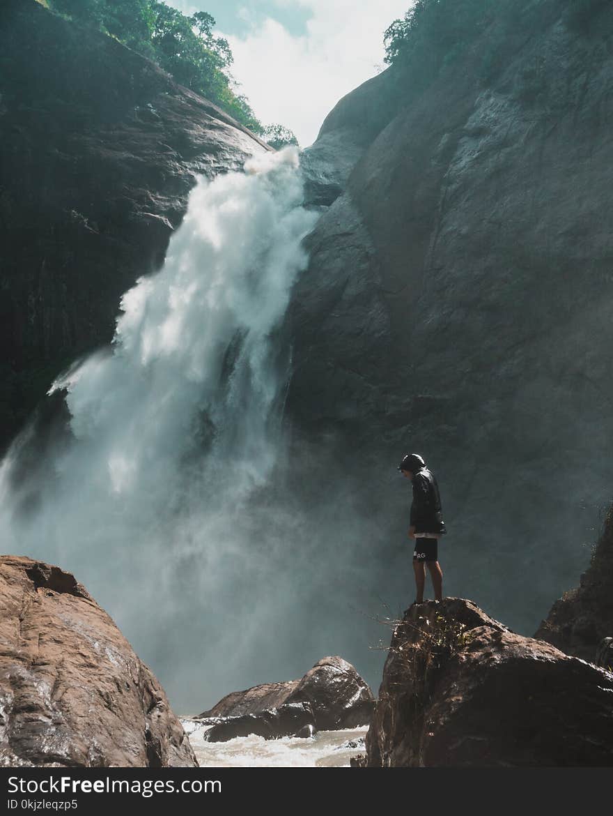 Man Standing on Brown Rock Cliff in Front of Waterfalls. Photographer: Oliver Sj�str�m,. Man Standing on Brown Rock Cliff in Front of Waterfalls. Photographer: Oliver Sj�str�m,