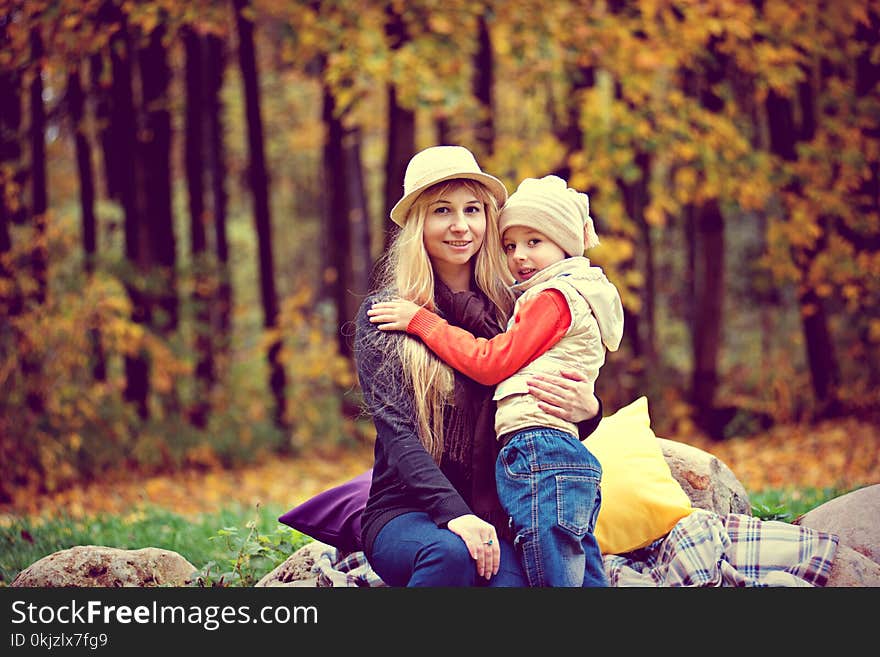 Woman Wearing Purple Long-sleeved Shirt Hugging Girl Wearing White Jacket Near Trees at Daytime