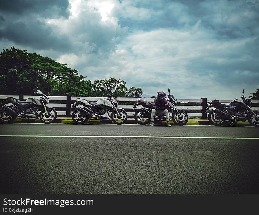 Man on Asphalt Road Sitting Beside Sports Bike Under White Clouds Blue Skies Daytime