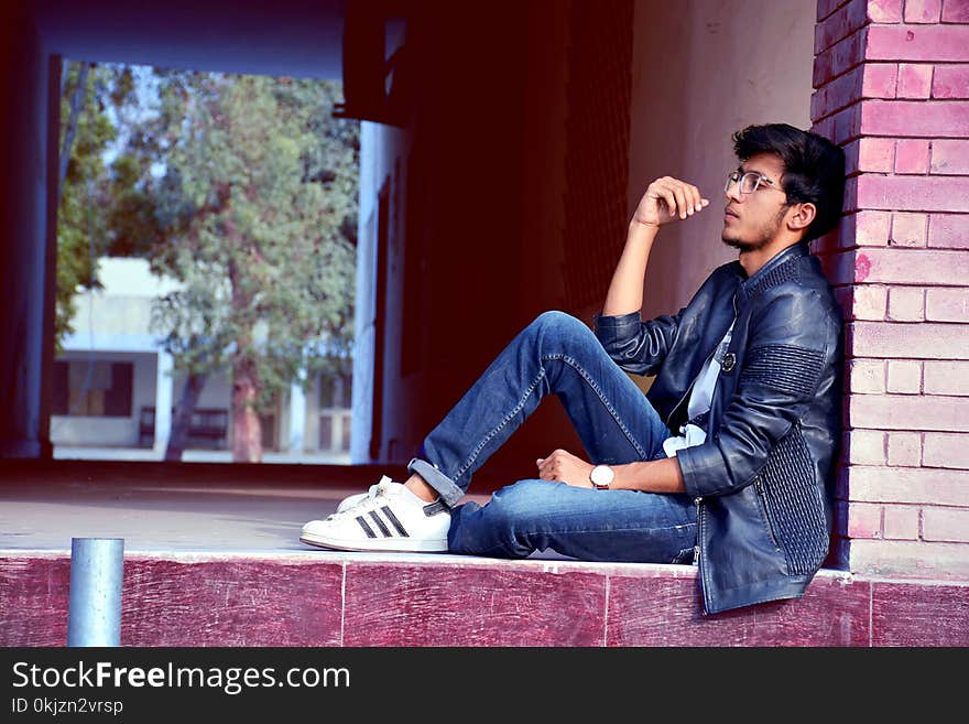 Man Wearing Black Leather Jacket and Blue Jeans Sitting on Floor