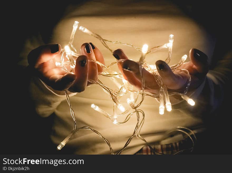 Closeup Photo of Person Wearing White Long-sleeved Shirt Holding Turned on String Lights