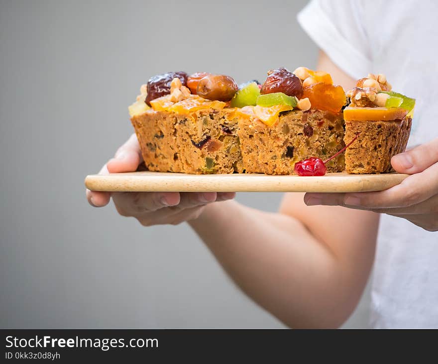 Female Hand Holding A Loaf Of Fruit Cake On Wooden Plate