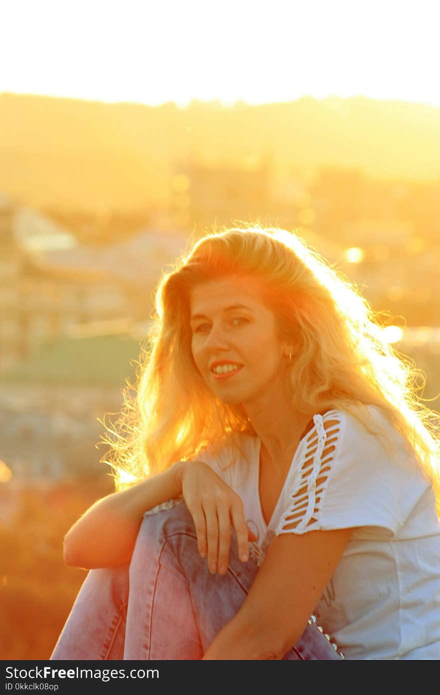 Smiling blonde girl in the sunlight, cityscape background.