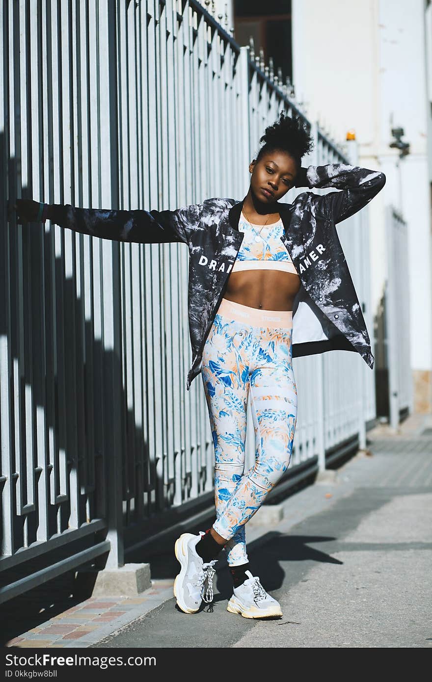 Woman in White Crop Top With Blue Full-zip Jacket and Blue Leggings Posing Near Gray Steel Fence