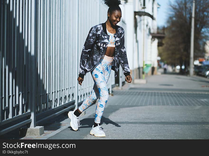 Woman Wearing Black Jacket and White Pants Standing on Grey Concrete Pavement