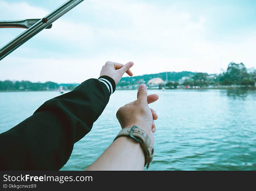 Two Person&#x27;s Left Hand Making Finger Heart Sign Near Body of Water