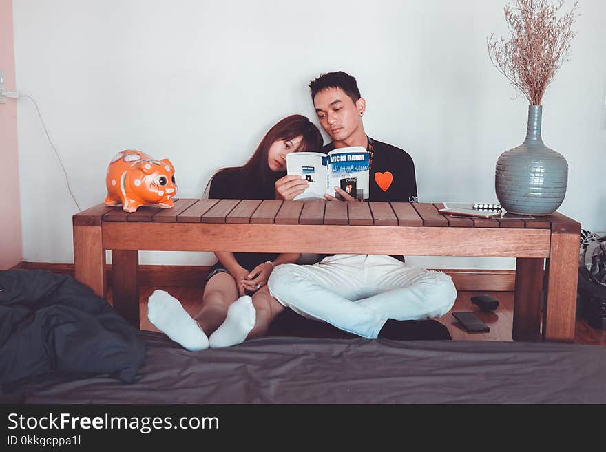 Couple Reading Book Sitting on Front of Rectangular Brown Wooden Coffee Table