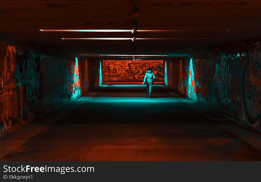 Person Wearing Jacket Walking on Tunnel With Red and Green Lights