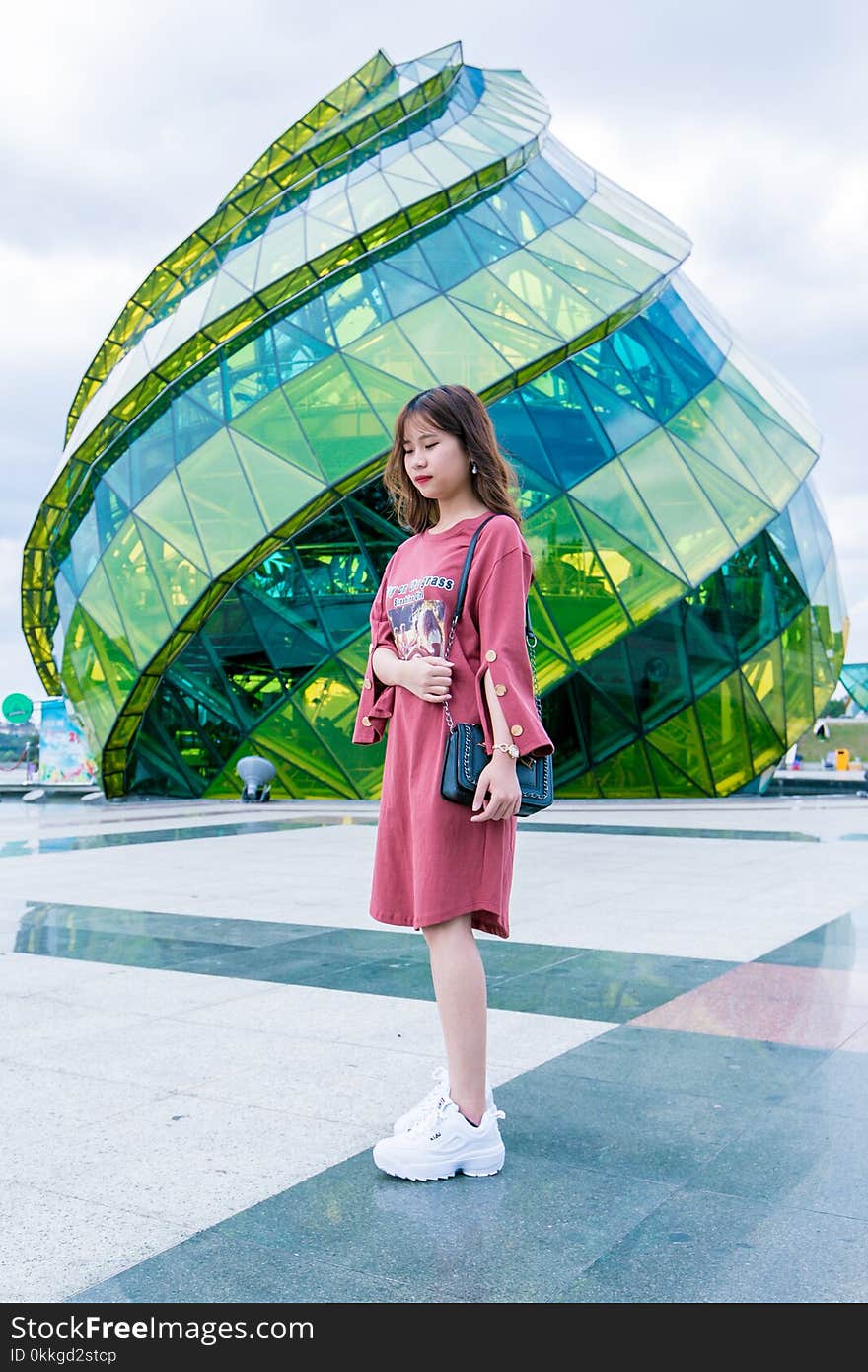 Girl Wearing Red Long-sleeved Dress and White Low-top Shoes Standing Near Green Glass Structure