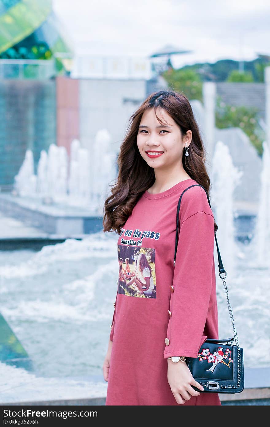 Woman in Purple Dress Carrying Bag Beside Water Fountain