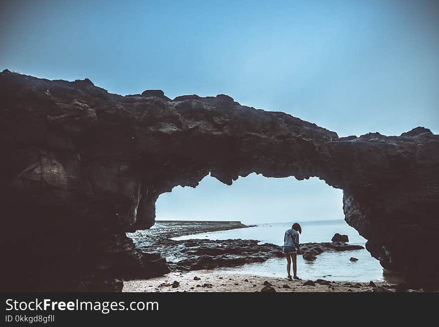 Person Standing on Beach Under Rock