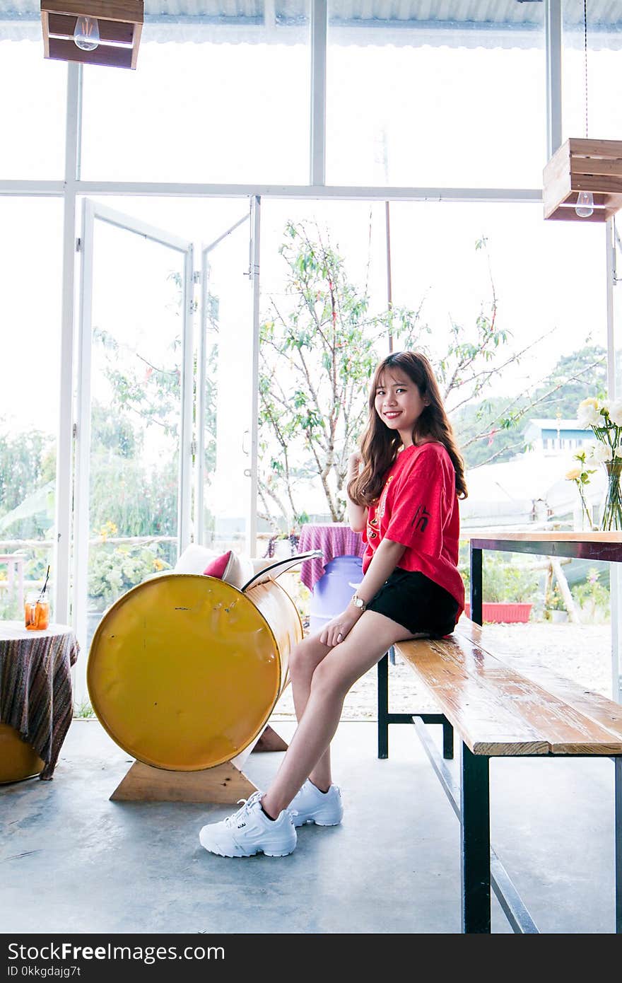 Woman Wearing Red Blouse and Black Short While Sitting on Table