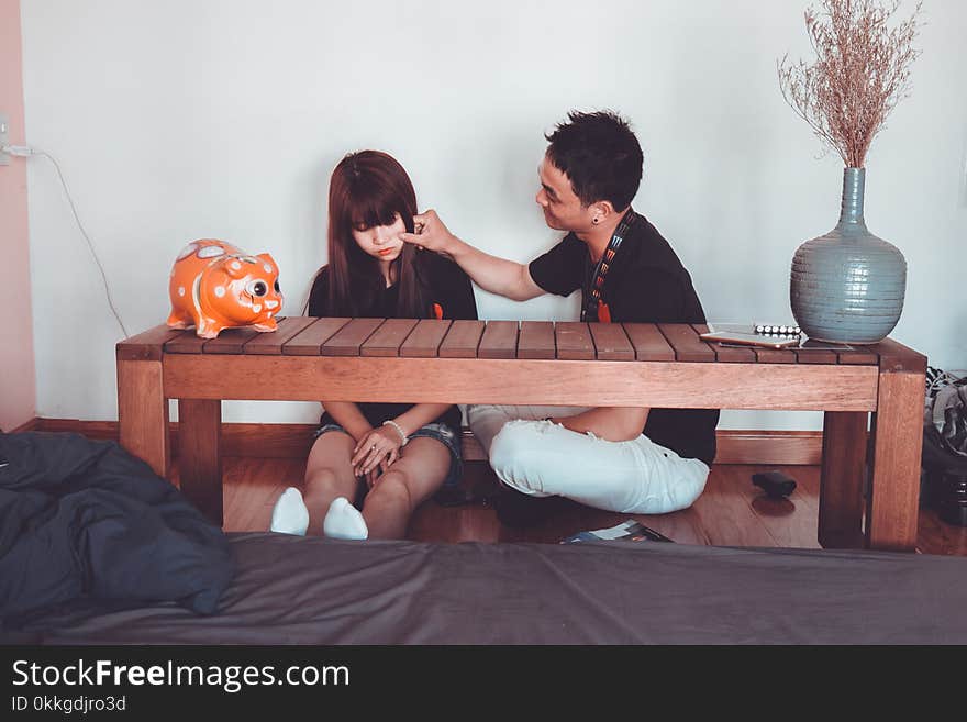 Man Pinching the Cheek of Woman Sitting Near Rectangular Brown Wooden Coffee Table