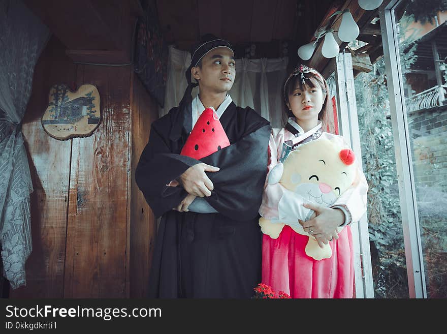 Man and Woman Holding Plush Toys Standing on Front of Brown Wall