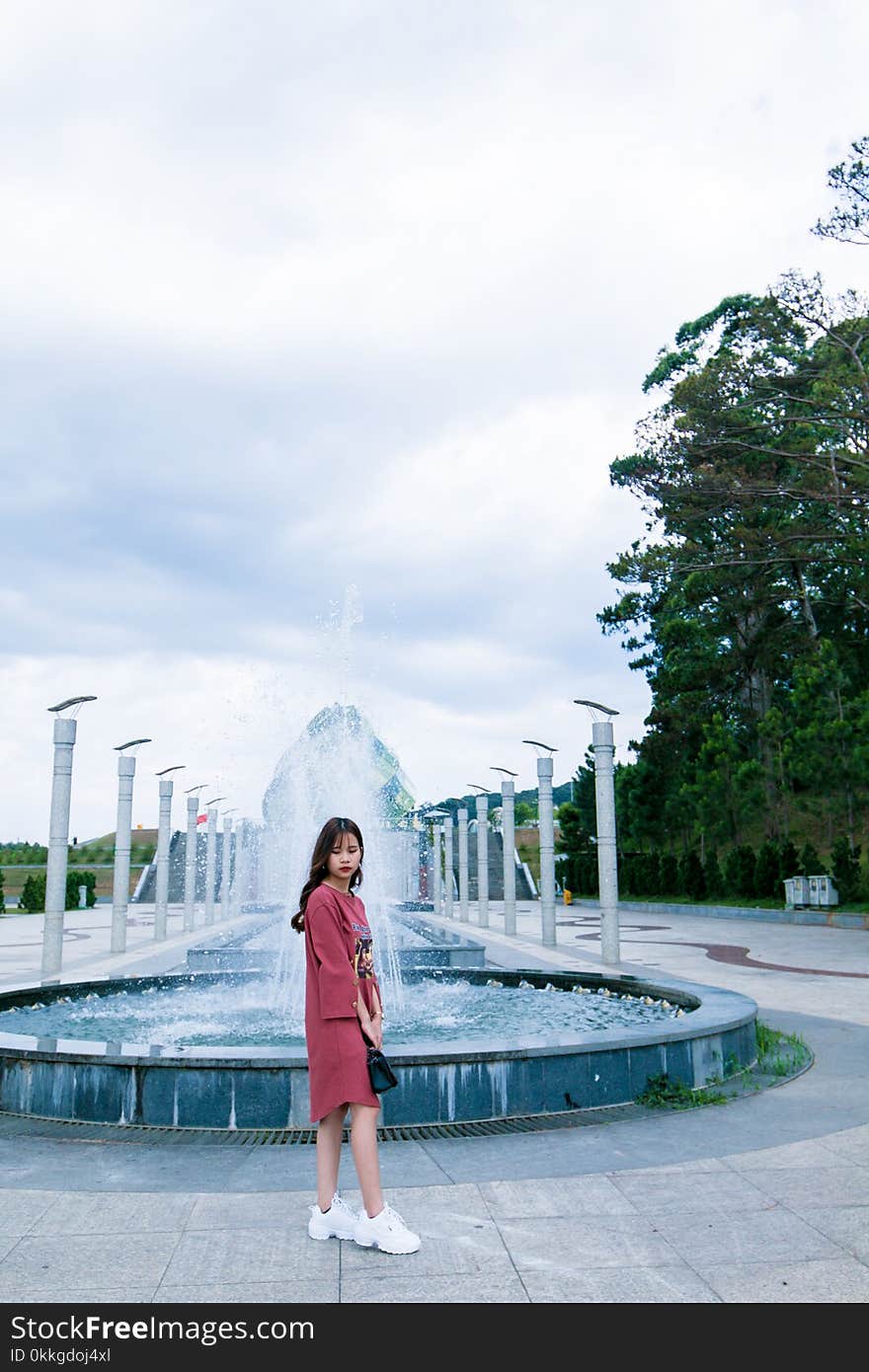 Woman in Red Long-sleeved Dress Standing Near Water Fountain at Daytime